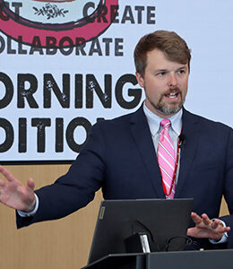 UNeMed Business Development Manager and Morning Edition organizer Tyler Scherr, PhD, addresses the gathering during brief welcoming remarks at the April 30, 2026, installment of Idea Pub: Morning Edition in the Forge Event Hall at Catalyst Omaha in the Edge District.