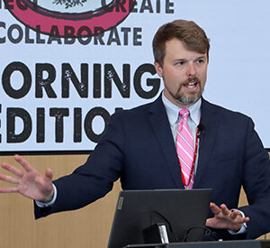 UNeMed Business Development Manager and Morning Edition organizer Tyler Scherr, PhD, addresses the gathering during brief welcoming remarks at the April 30, 2026, installment of Idea Pub: Morning Edition in the Forge Event Hall at Catalyst Omaha in the Edge District.