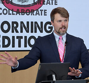 UNeMed Business Development Manager and Morning Edition organizer Tyler Scherr, PhD, addresses the gathering during brief welcoming remarks at the April 30, 2026, installment of Idea Pub: Morning Edition in the Forge Event Hall at Catalyst Omaha in the Edge District.